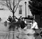 Residents leave their flooded Nebraska neighborhood homes on March 14, 1982. This view is from the West Main Street bridge looking west. Being resourceful, the people in the second boat are using snow shovels as paddles.