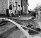 Residents watch water from their homes being pumped out into the street as the floodwaters subside.